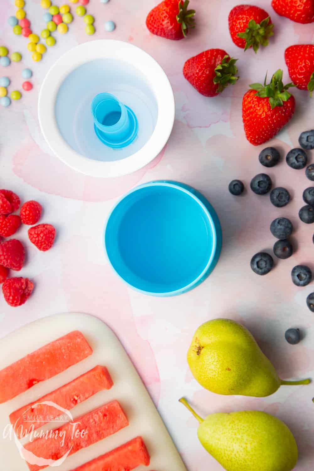 YoPop frozen yogurt maker laid out on a pink surface surrounded by fruit.