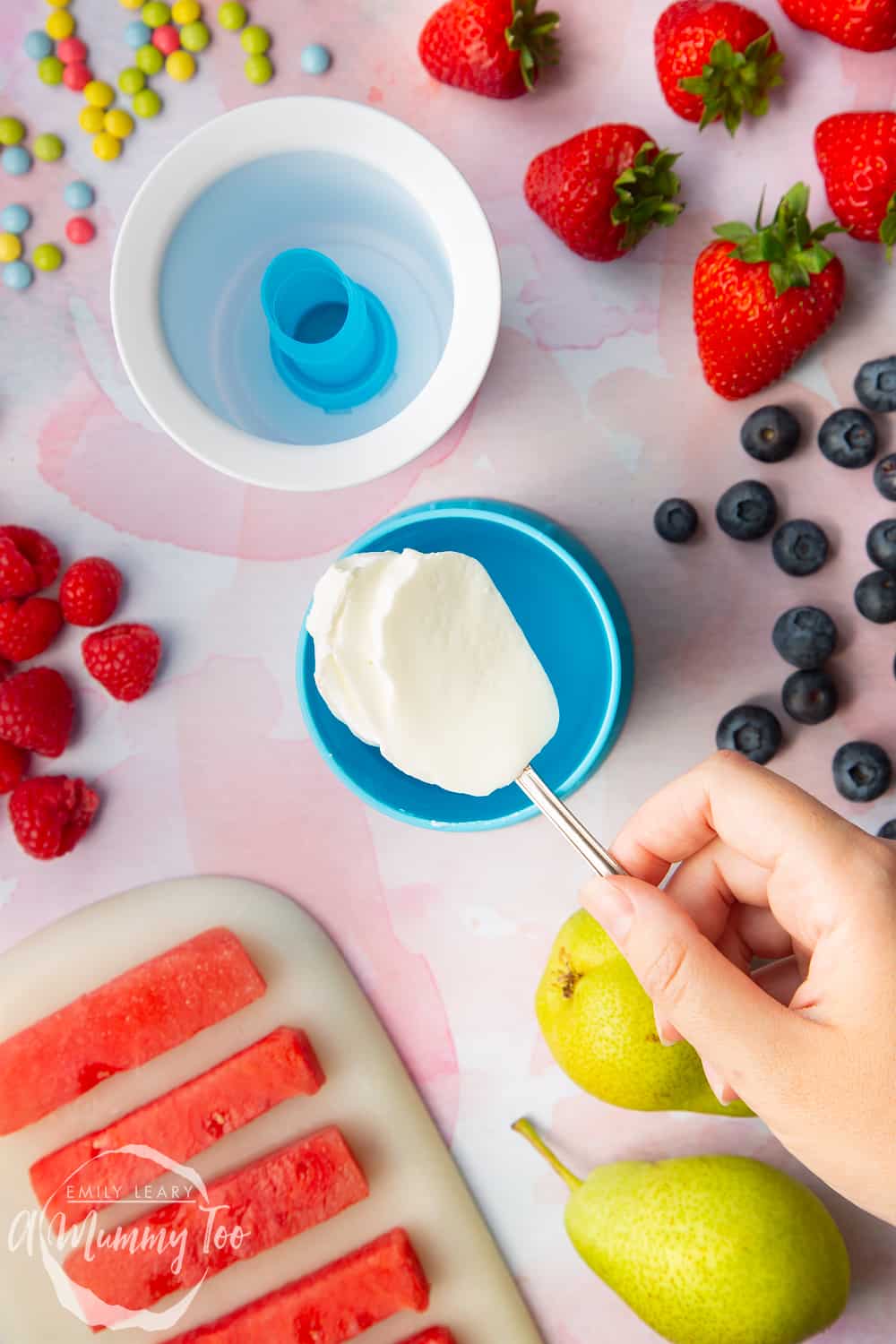 YoPop frozen yogurt maker laid out on a pink surface surrounded by fruit with fresh yogurt in a dish