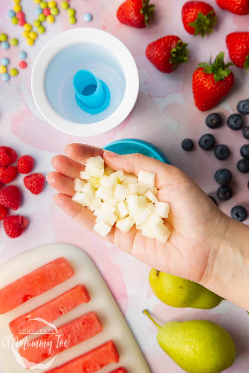 YoPop frozen yogurt maker open with a hand holding small pieces of pear with more fruit in the background.