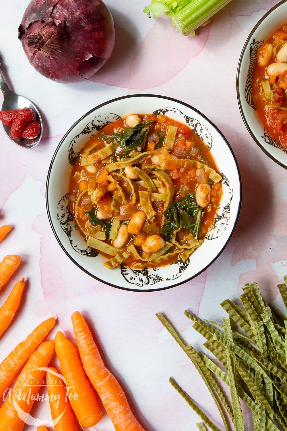 A bowl of hot pasta e fagioli surrounded by the ingredients used to make it.