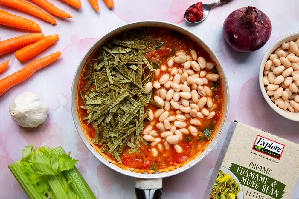 A frying pan containing the sauce with the fettuccine pasta and cannellini beans added.