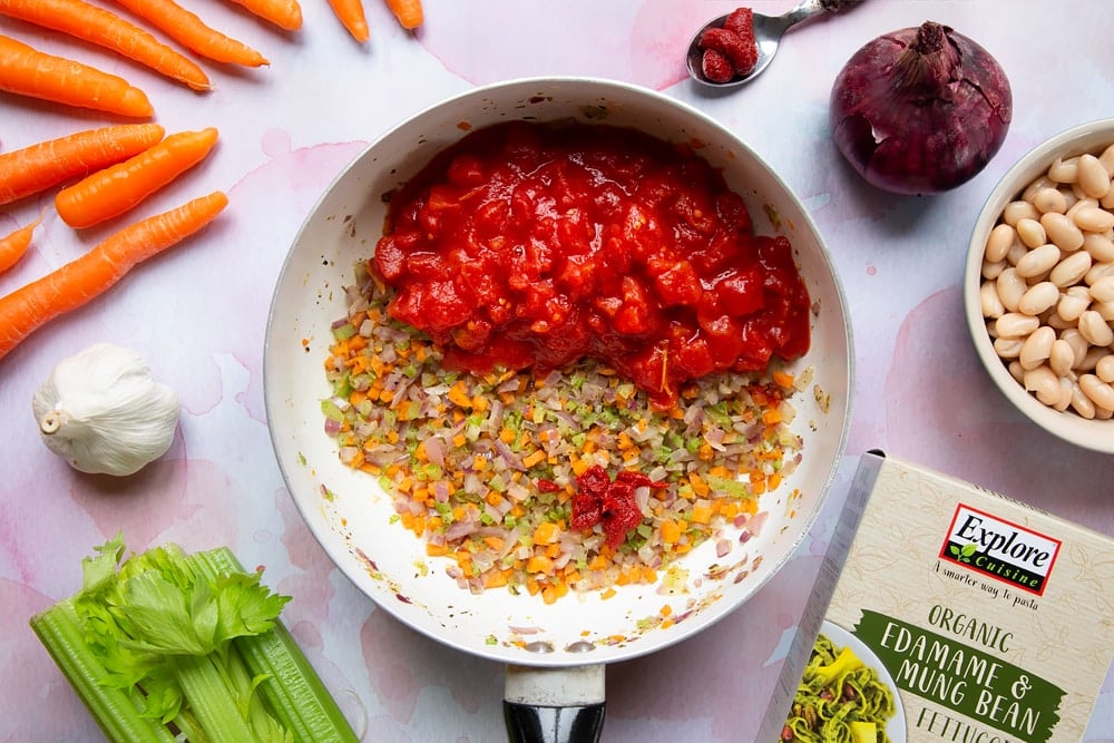 A tin of tomatoes and the tomato puree added to the cooked carrots, celery, onion, garlic, oregano, salt and pepper in a frying pan.