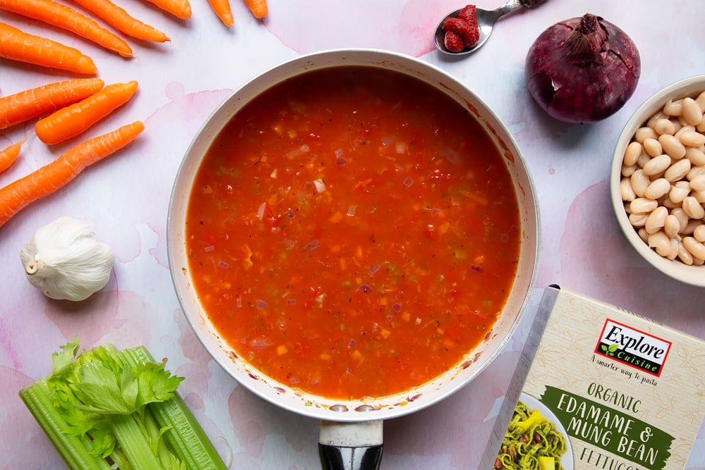 Vegetable stock added to a tin of tomatoes, tomato puree, cooked carrots, celery, onion, garlic, oregano, salt and pepper in a frying pan.