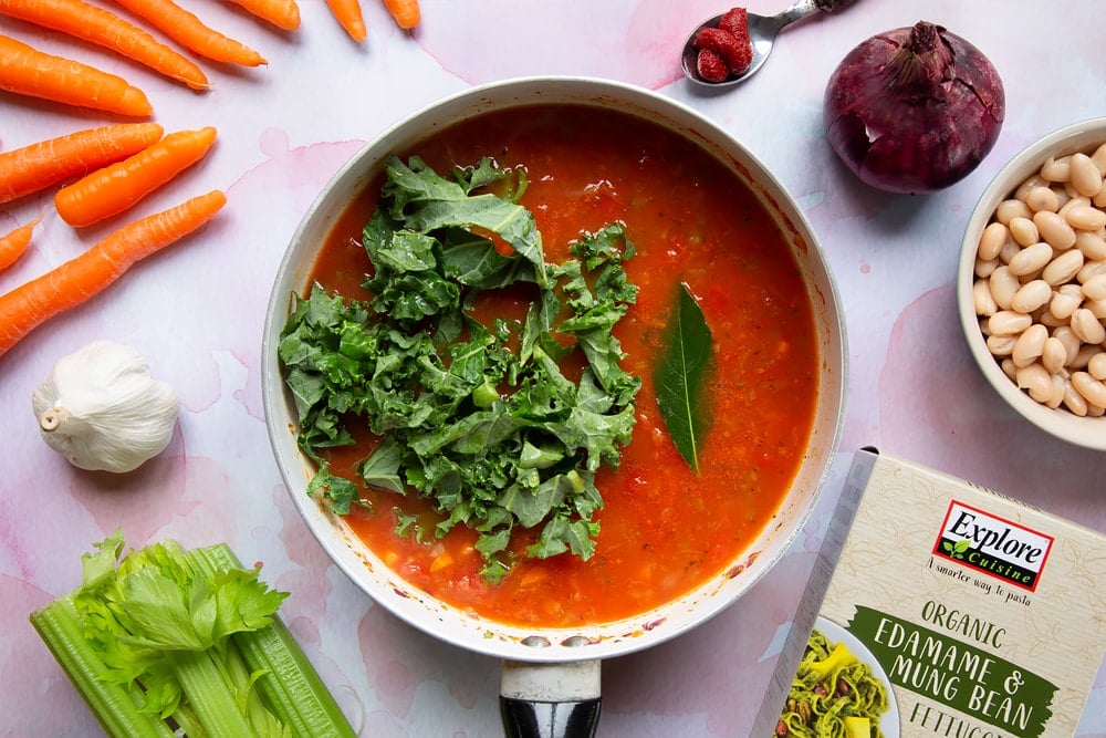 Kale and bay leaf added to the vegetable stock, tin of tomatoes, tomato puree, cooked carrots, celery, onion, garlic, oregano, salt and pepper in a frying pan.