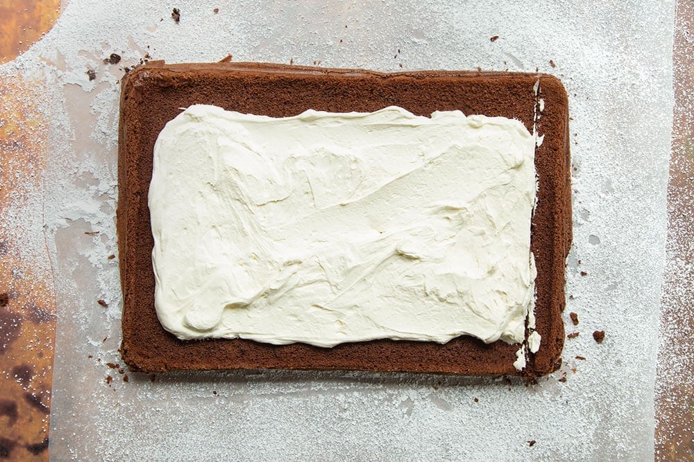 Chocolate roulade sponge cooked and turned out onto baking paper - the surface of the sponge spread with whipped cream.