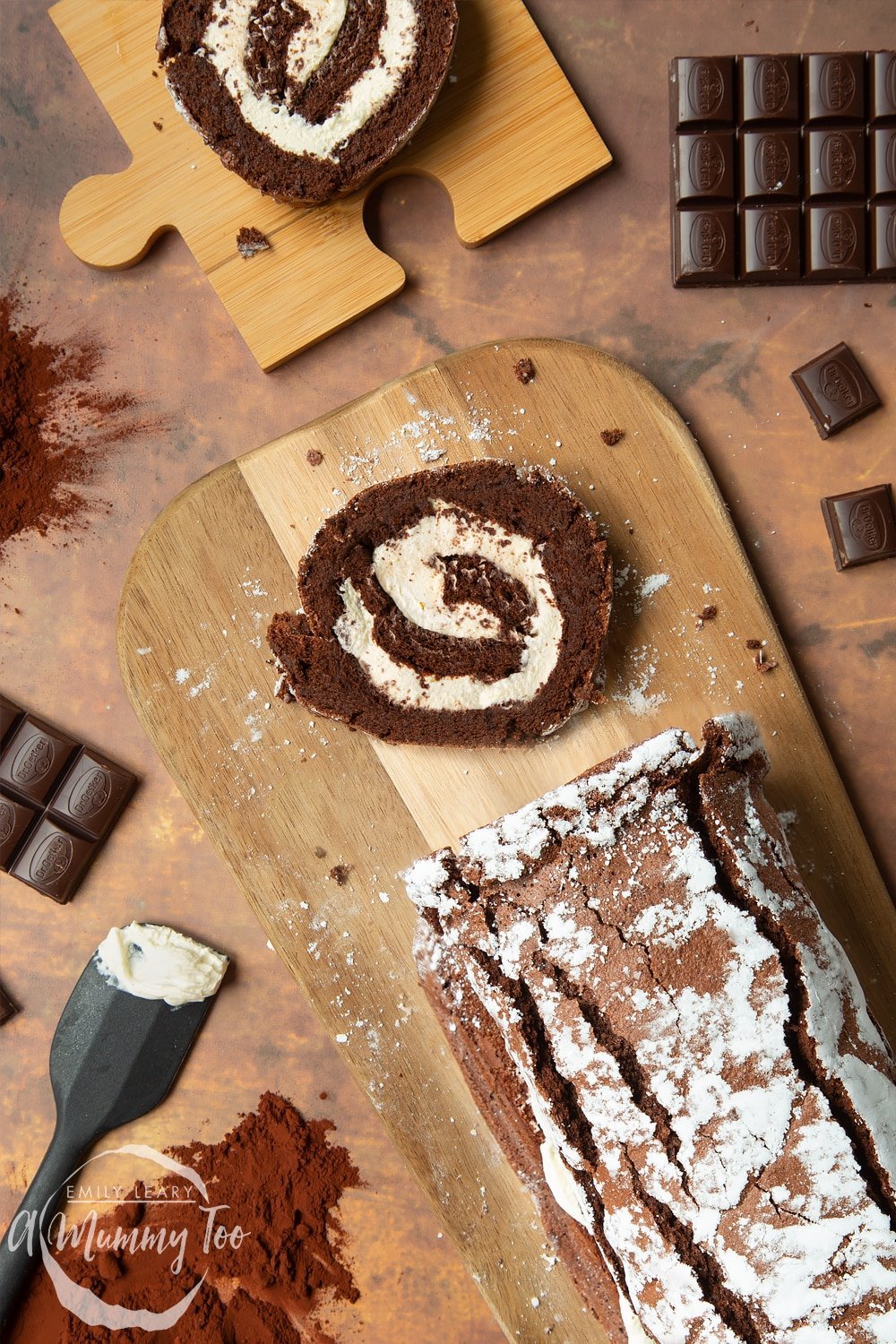Mary Berry's chocolate roulade arranged on a board with one slice cut out. Ingredients are scattered around the board.
