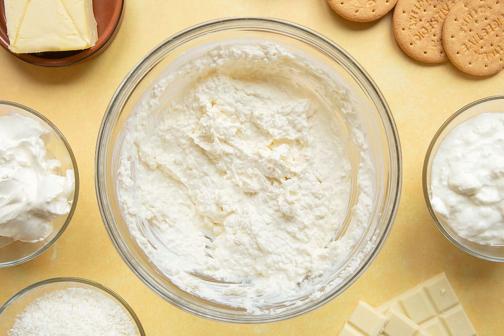 Cream cheese and yogurt whisked together in a large mixing bowl, combined with desiccated coconut.