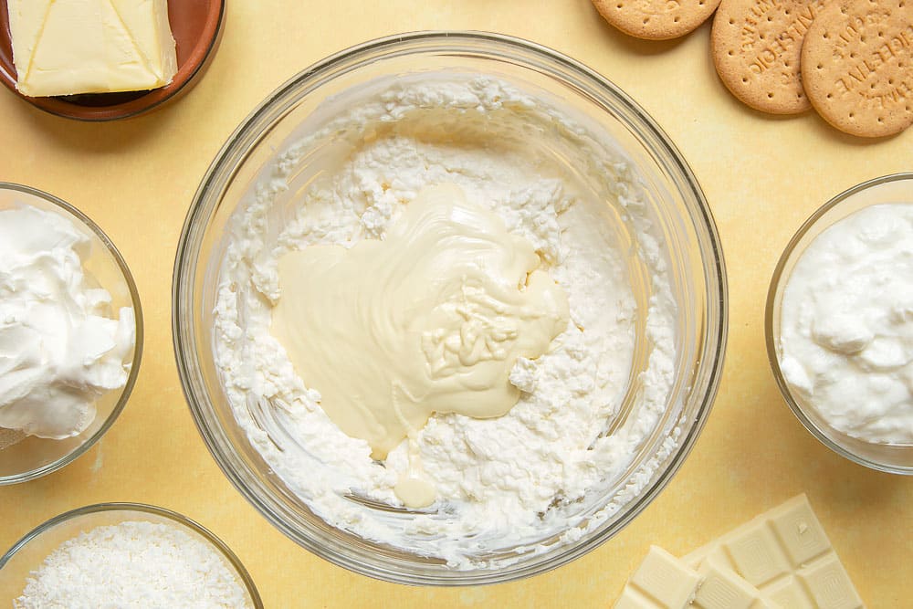 Cream cheese, yogurt and desiccated coconut combined in a large mixing bowl. Melted white chocolate on top.