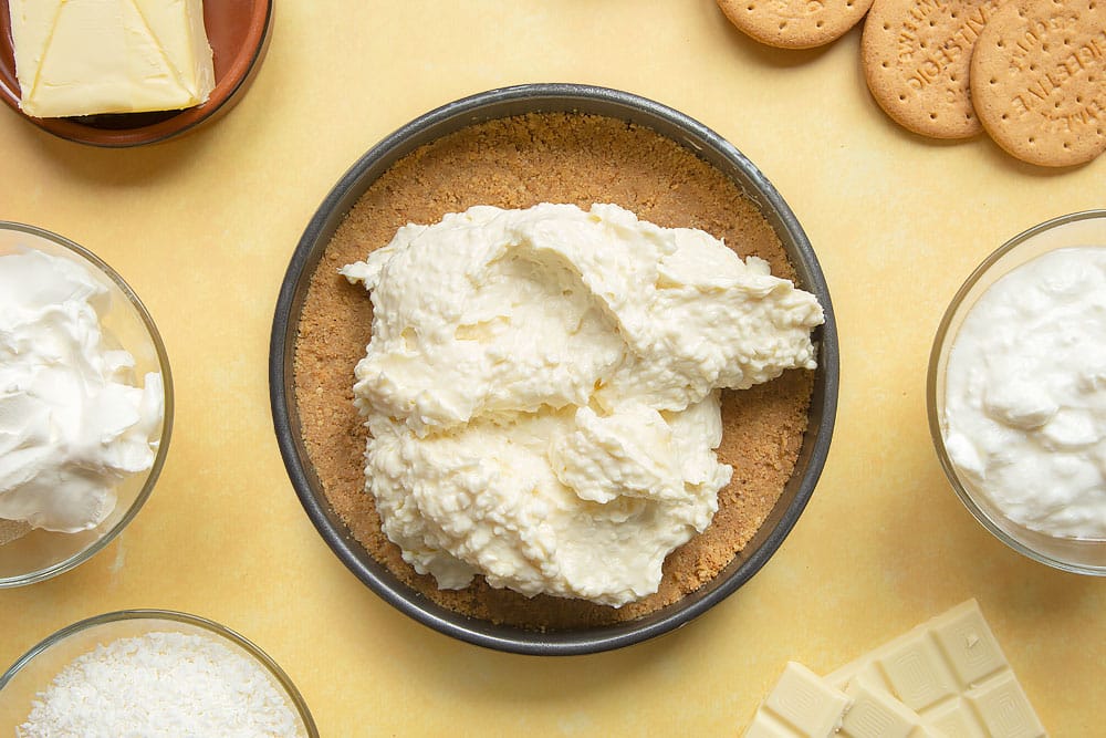 Cream cheese, yogurt, desiccated coconut and melted white chocolate mix added to a cake tin with a biscuit base.