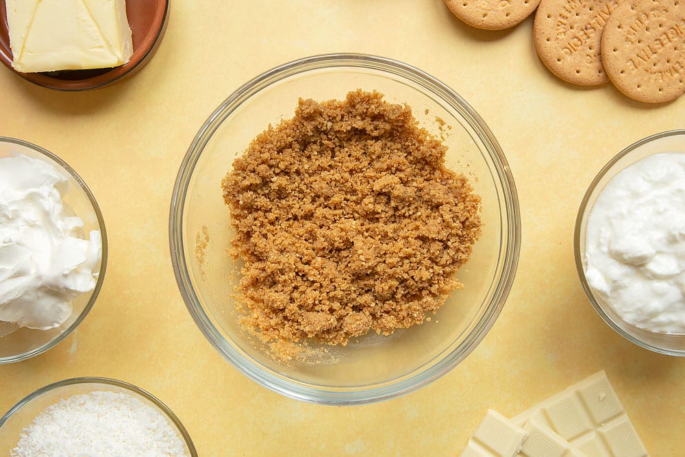 Crushed biscuits combined with melted butter in a mixing bowl.