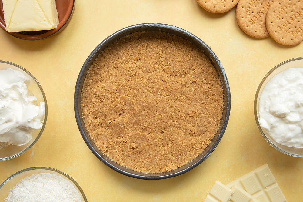 Crushed biscuits combined with melted butter pressed into the base of a greased cake tin.