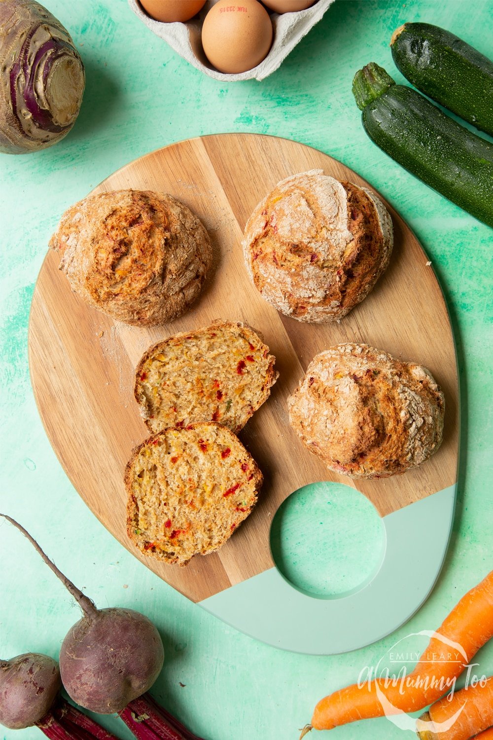 Vegetable soda bread rolls recipe - rolls arranged on a board, one cut open to show the vegetable flecked interior. Surrounded by vegetables.
