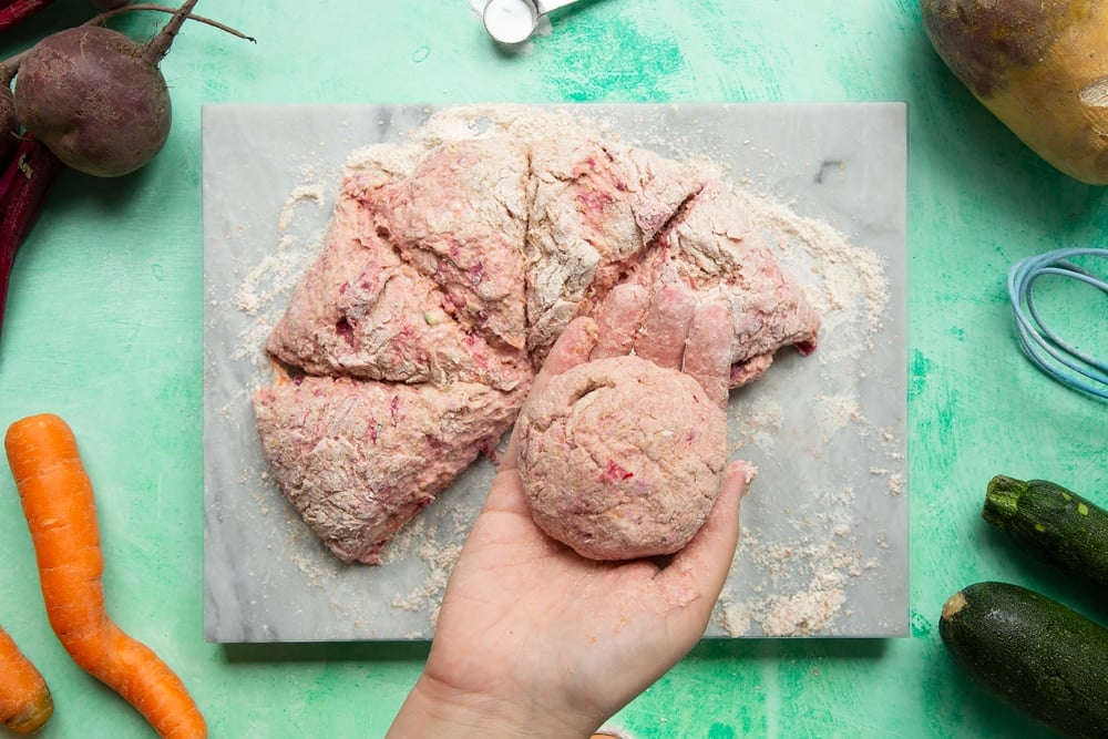 Vegetable soda bread rolls recipe - the pink dough being rolled into balls in a hand.