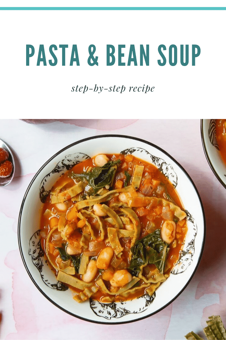 A bowl of hot pasta e fagioli with all the ingredients peeking out the sauce. Some raw ingredients are visible on the table.