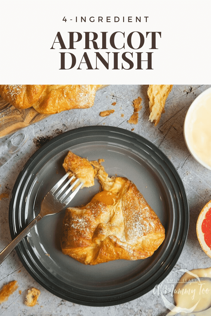 Overhead shot of a four ingredient apricot danish on a black plate with a fork on the side. The plate is sitting on a grey table with some additional ingredients required to make the danish on the side.