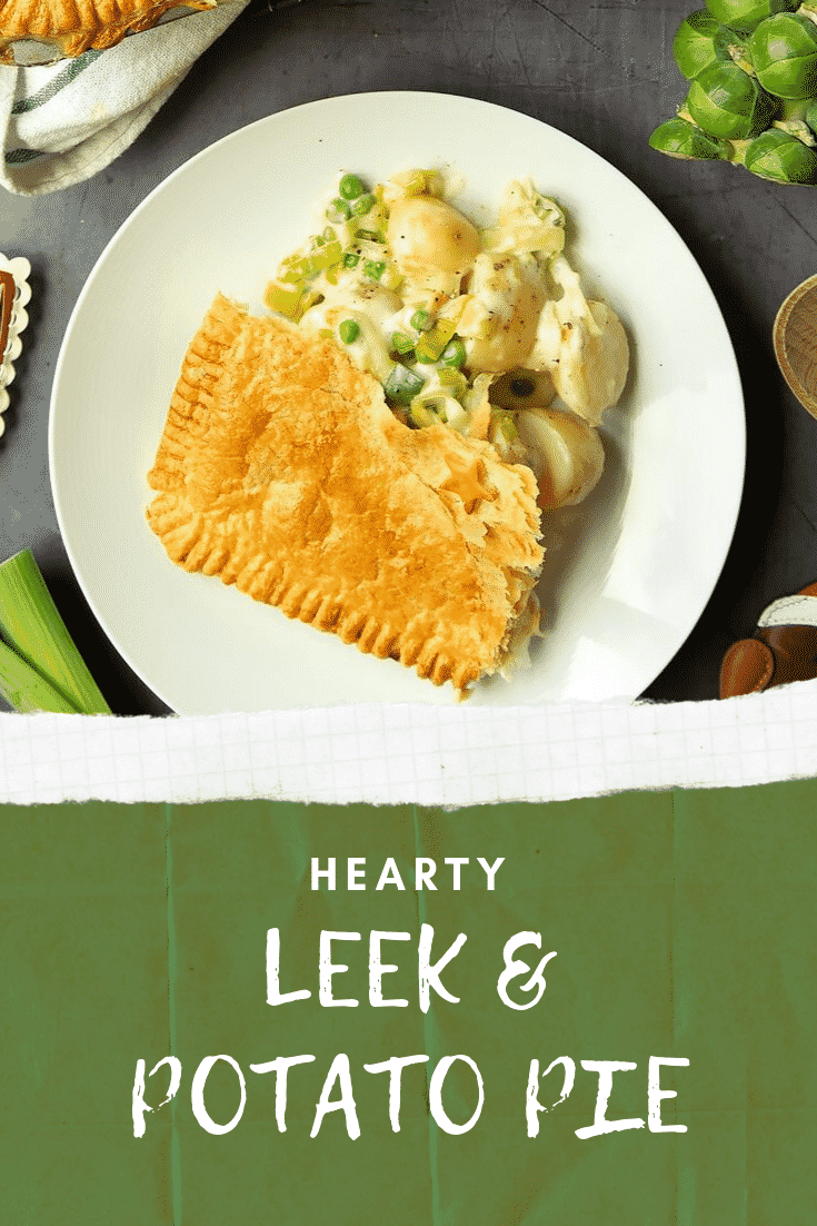Cheesy leek and potato pie on a plate. The plate is sat on a black surface surrounded by ingredients that are required to make the pie. At the bottom of the image there is some text describing the image for Pinterest. 