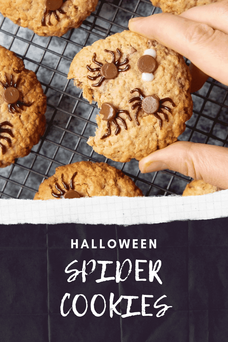 A hand is lifting up a Halloween peanut butter spider cookie from a cooling rack filled with them. A bite has been taken from from the cookie.