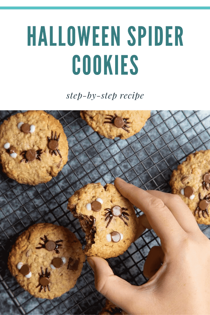 A hand is lifting up a Halloween peanut butter spider cookie from a cooling rack filled with them. A bite has been taken from from the cookie.