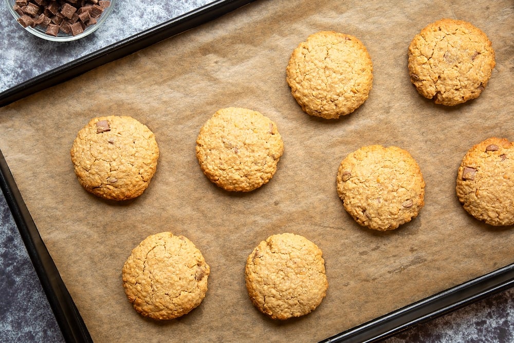 Eight baked and lightly golden brown Halloween peanut butter spider cookies on a baking sheet lined with baking paper.