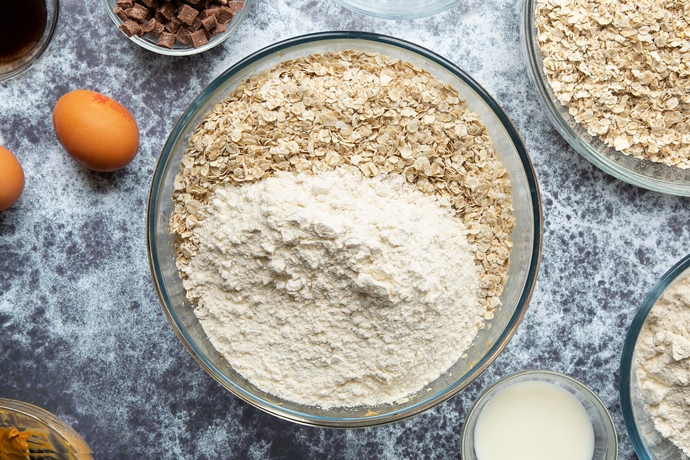 Flour and oats added to the bowl of whisked sugar, butter, peanut, eggs, milk and vanilla.