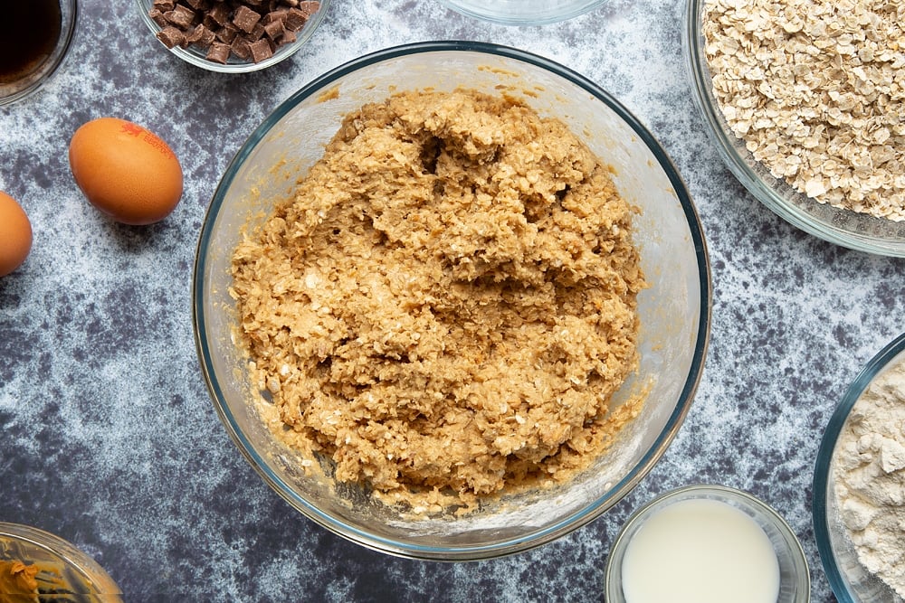 Flour, oats, sugar, butter, peanut, eggs, milk and vanilla combined in a mixing bowl to form the basic Halloween peanut butter spider cookie dough. 