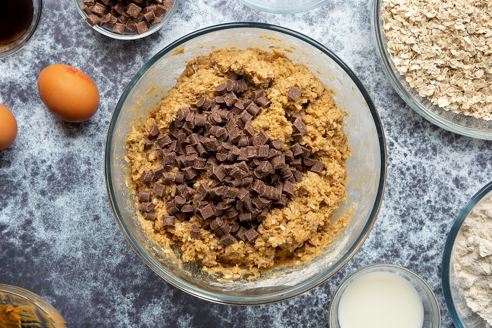 Chocolate chips on top of a mixture of flour, oats, sugar, butter, peanut, eggs, milk and vanilla, which form the basic Halloween peanut butter spider cookie dough. 