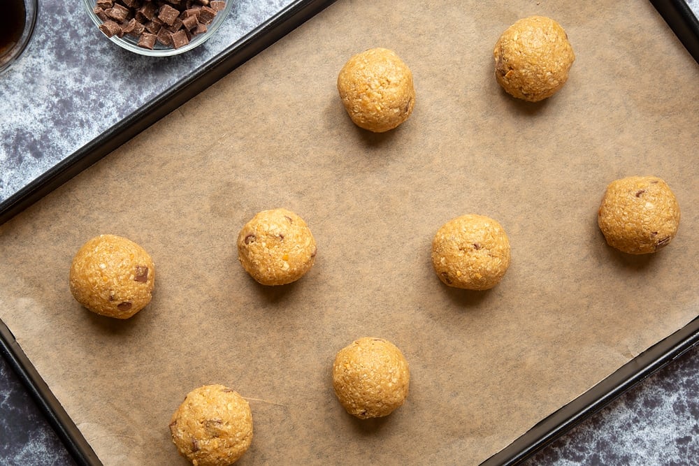 Eight raw Halloween peanut butter spider cookie dough balls on a baking sheet lined with baking paper.