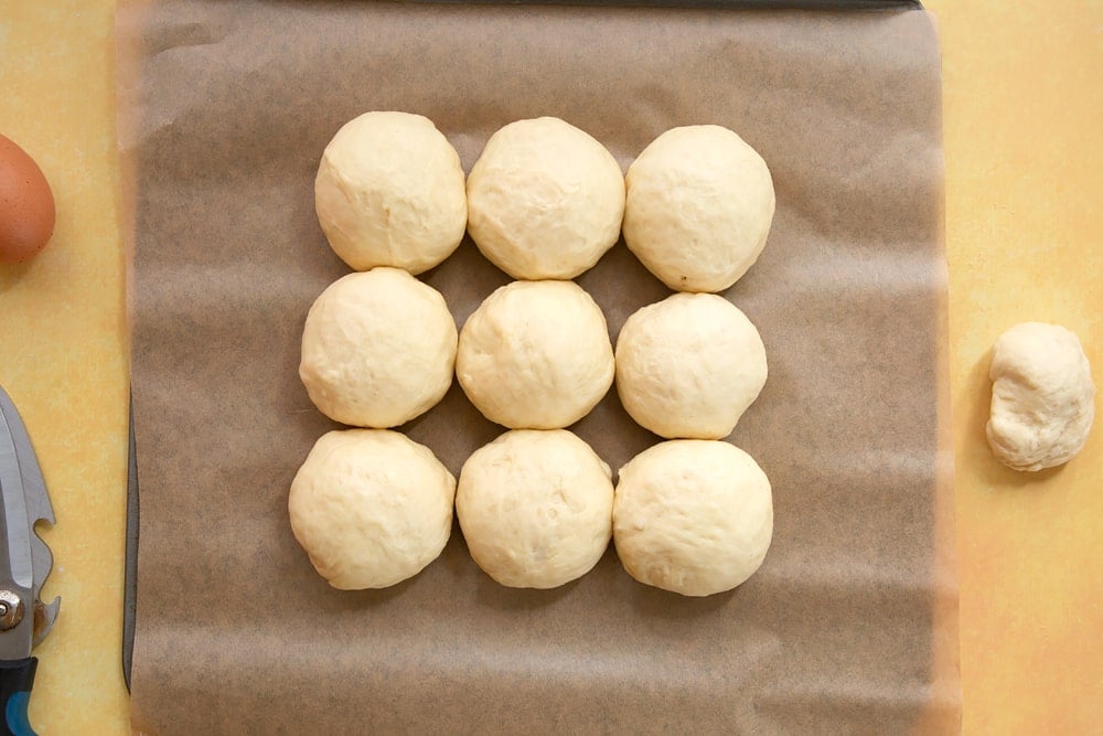 Tangzhong bread dough divided into  9 equally sized balls with a little dough left over. The 9 balls are arranged on a tray lined with baking paper