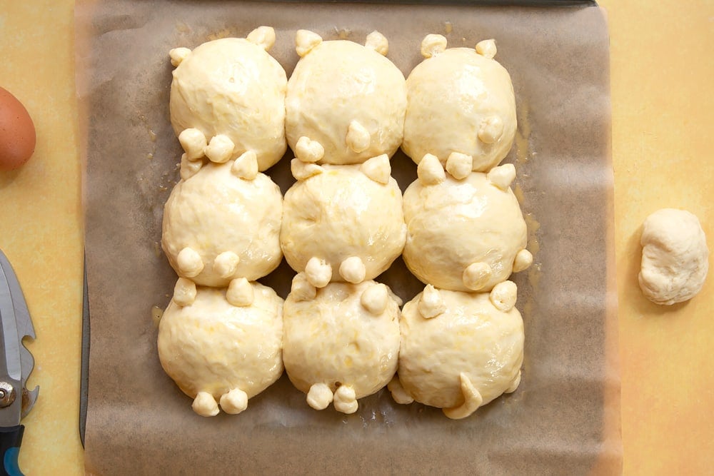 9 cat shaped tangzhong bread rolls on a tray lined with baking paper. Proved and brushed with egg wash.