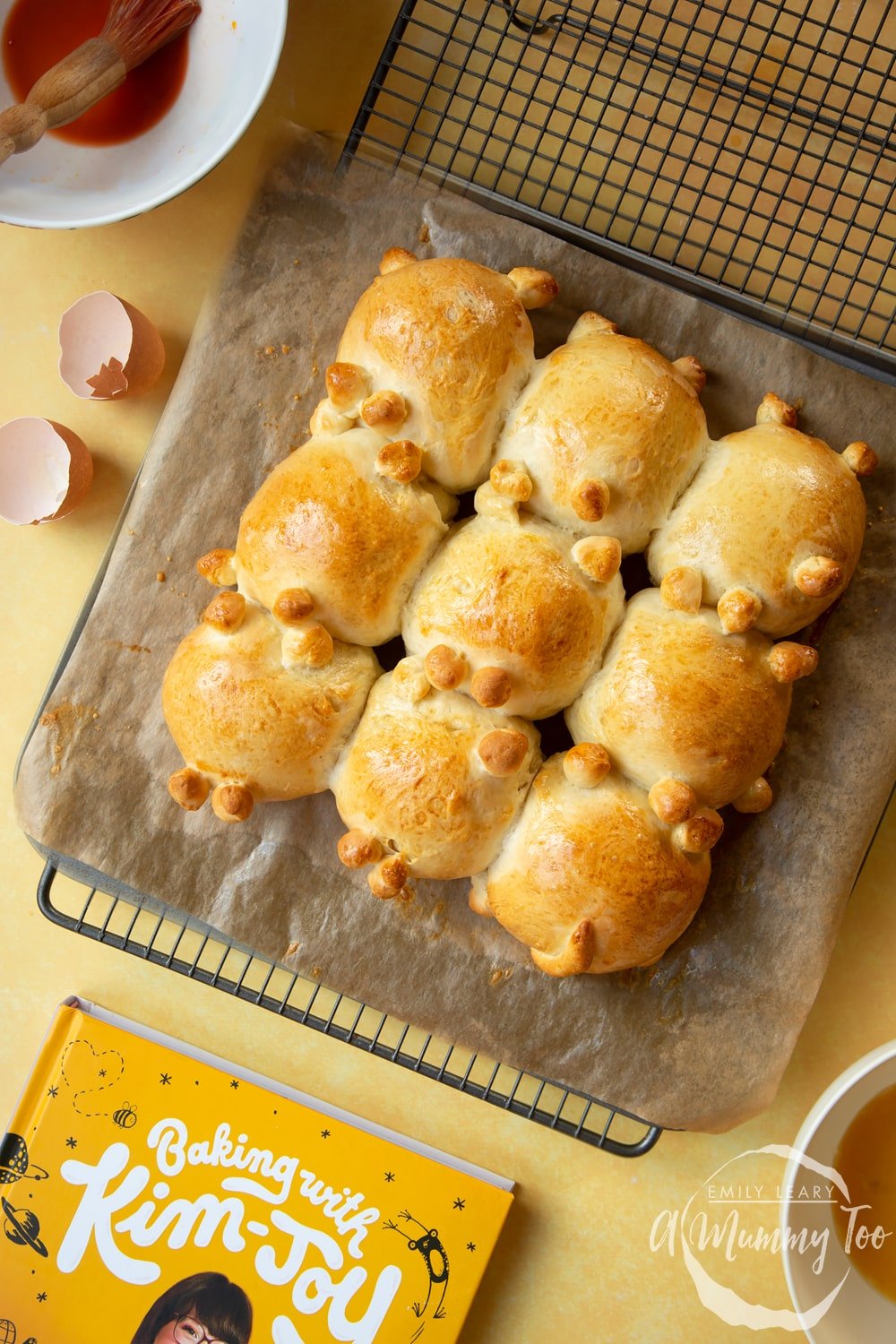 9 cat shaped tangzhong bread rolls on a tray lined with baking paper. Baked and cooling on a wire rack.