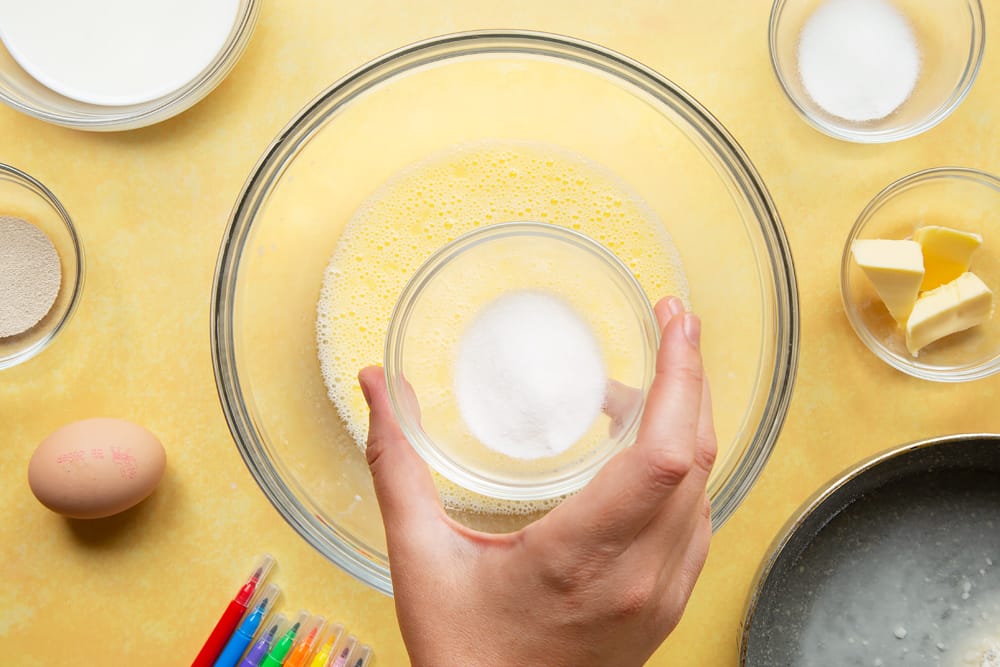 Adding sugar to warm milk and warm butter in a large bowl.