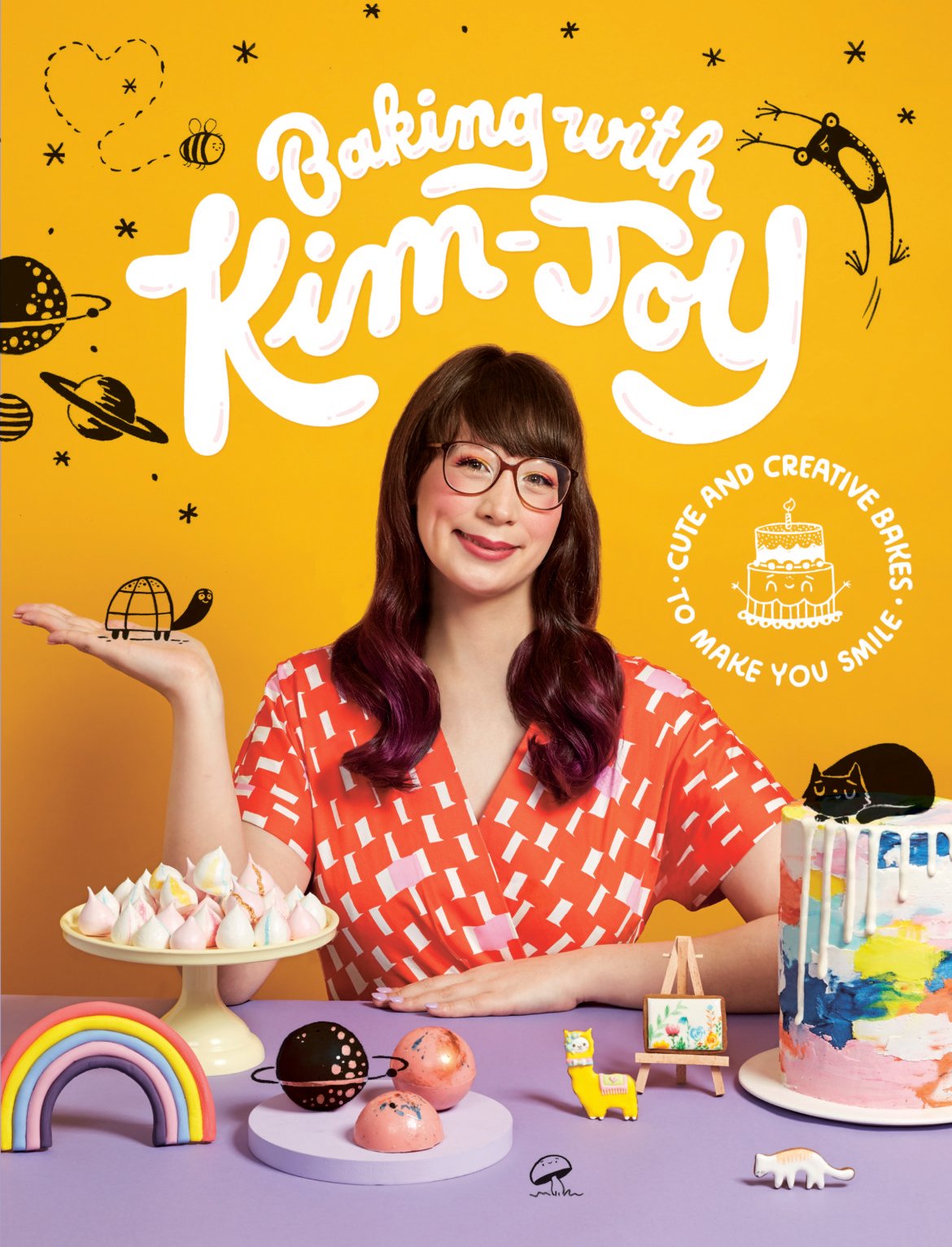 Book cover: Baking with Kim-Joy. Shows the author sitting at a table surrounded by her bakes