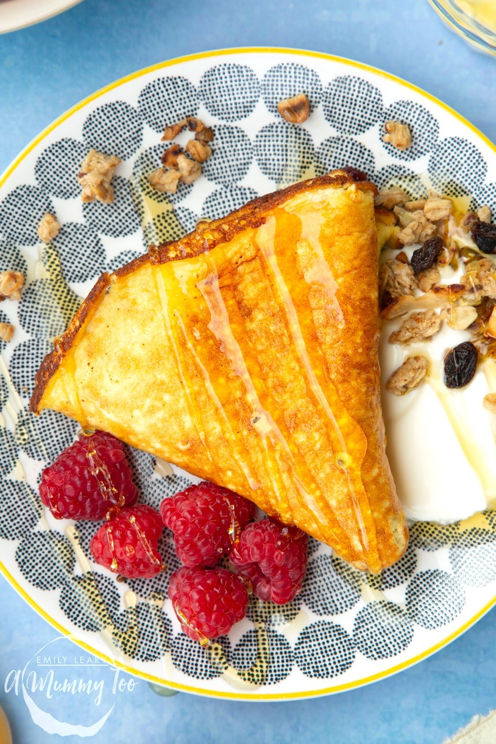 Sweet omelette served onto a plate with raspberries, yogurt, granola and honey