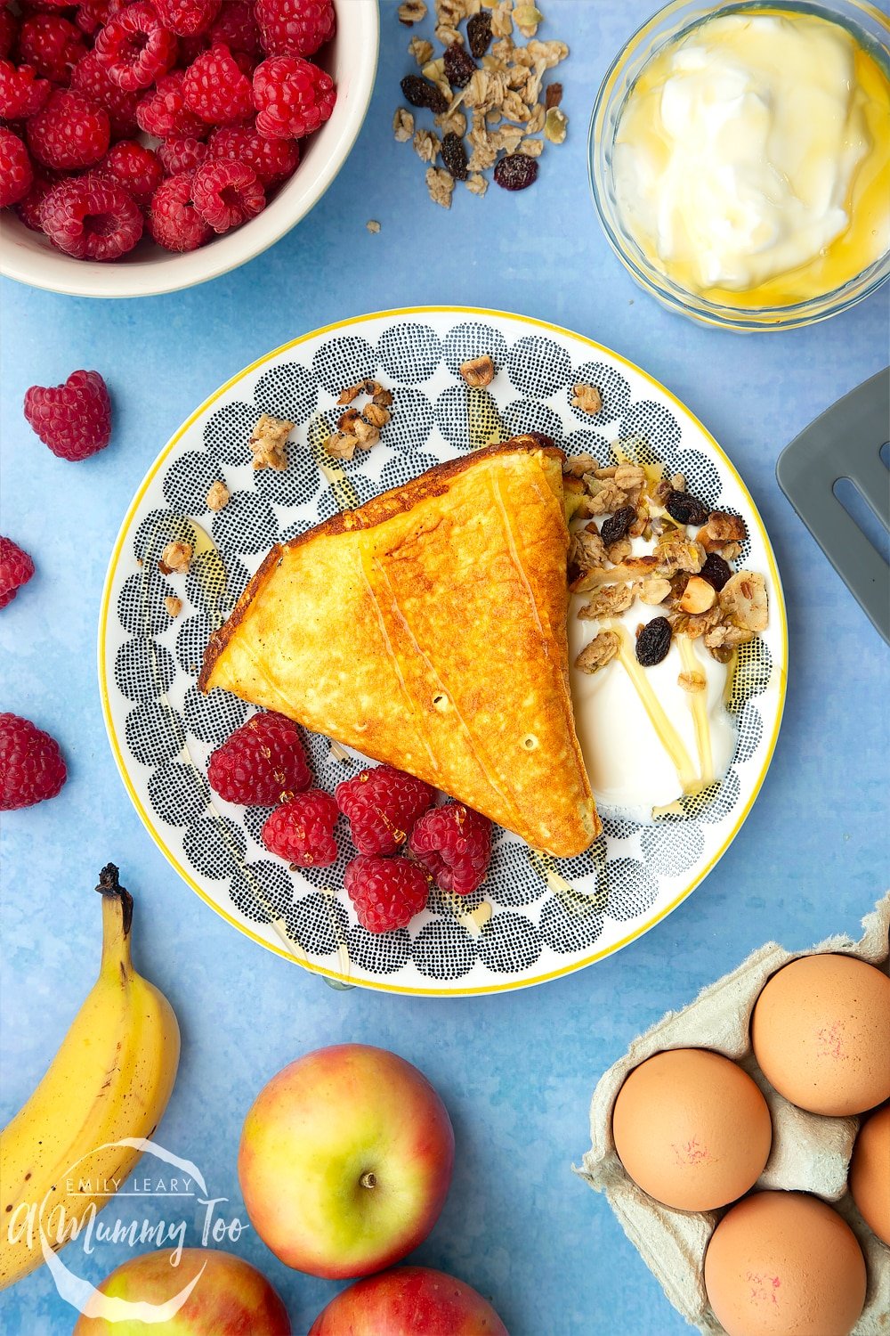 Sweet breakfast omelette on a plate with granola, yogurt and raspberries, drizzled with honey