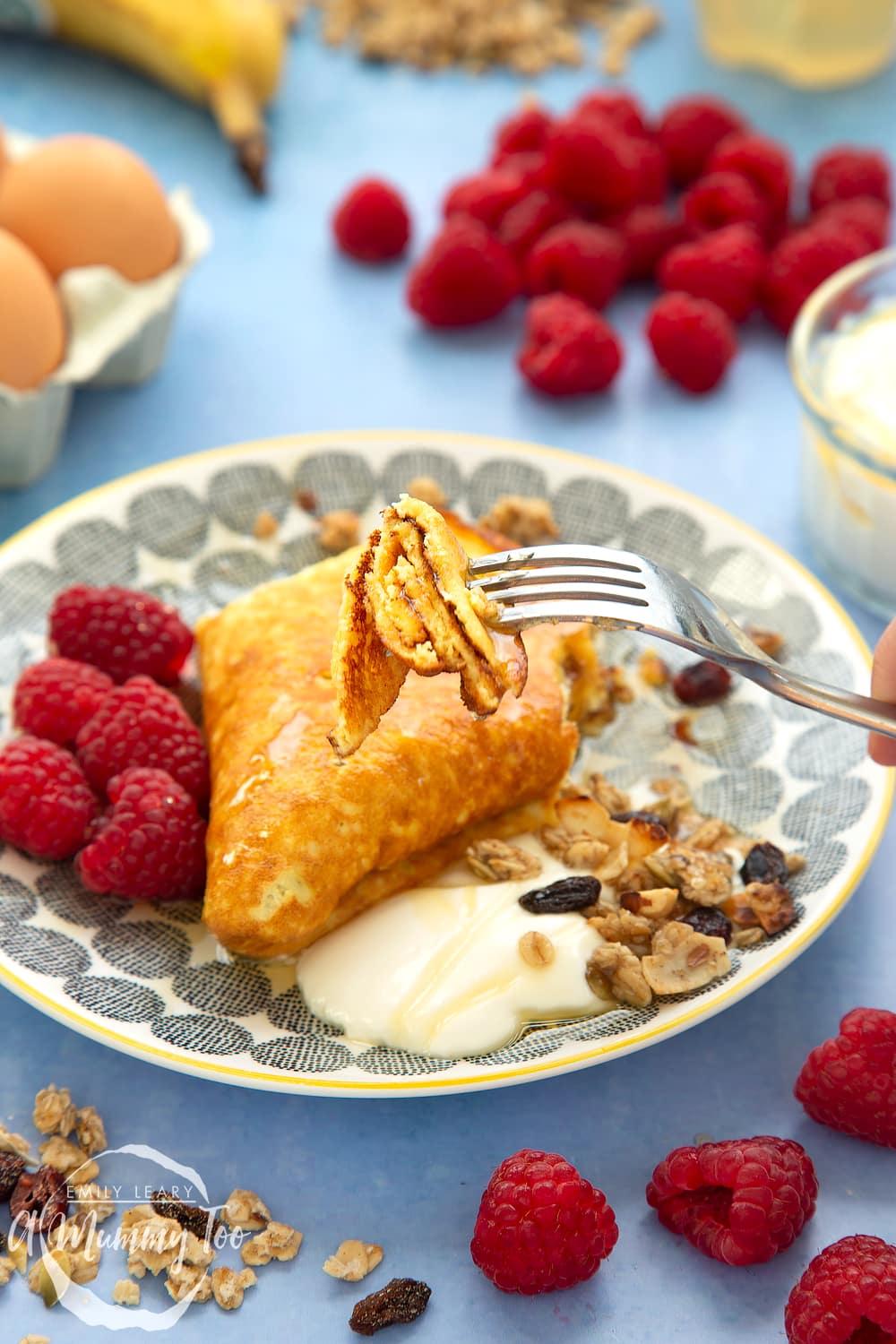 Sweet omelette served onto a plate with raspberries, yogurt, granola and honey. A piece of omelette on a fork