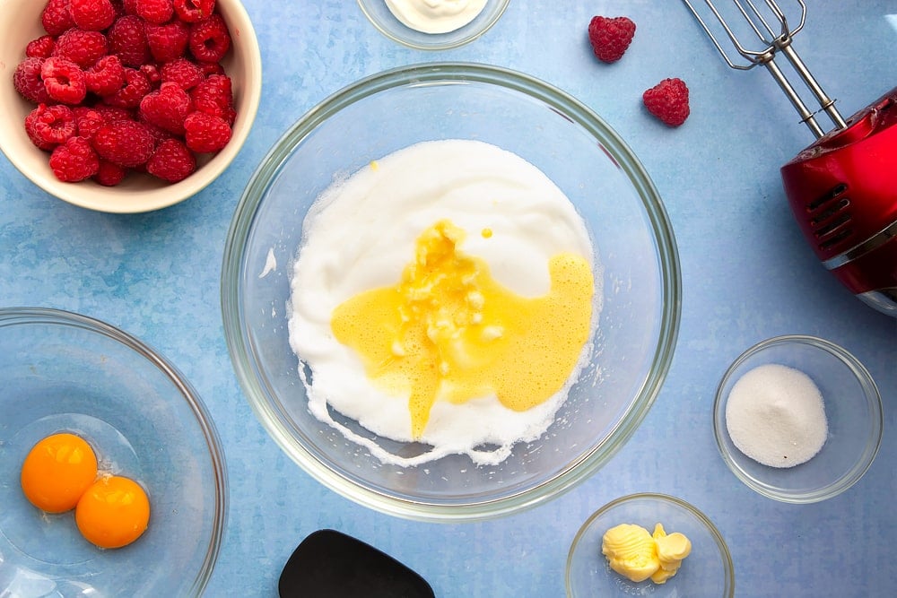Mixing bowl containing beaten egg whites, with a mix of egg yolks, yogurt and sugar poured on top