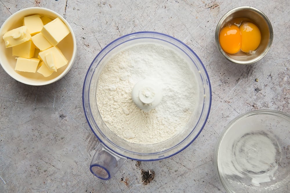 flour in a blender bowl along with 2 other bowls with eggs and butter inside.