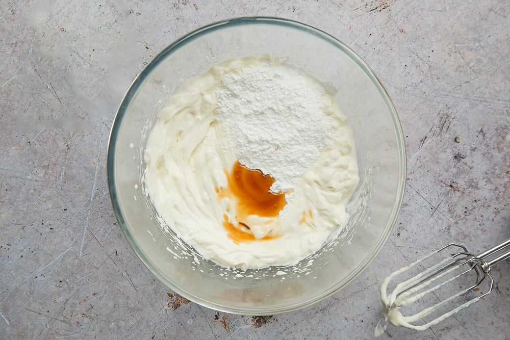 yogurt, sugar and vanilla essence in a large clear bowl with a whisk on the side.