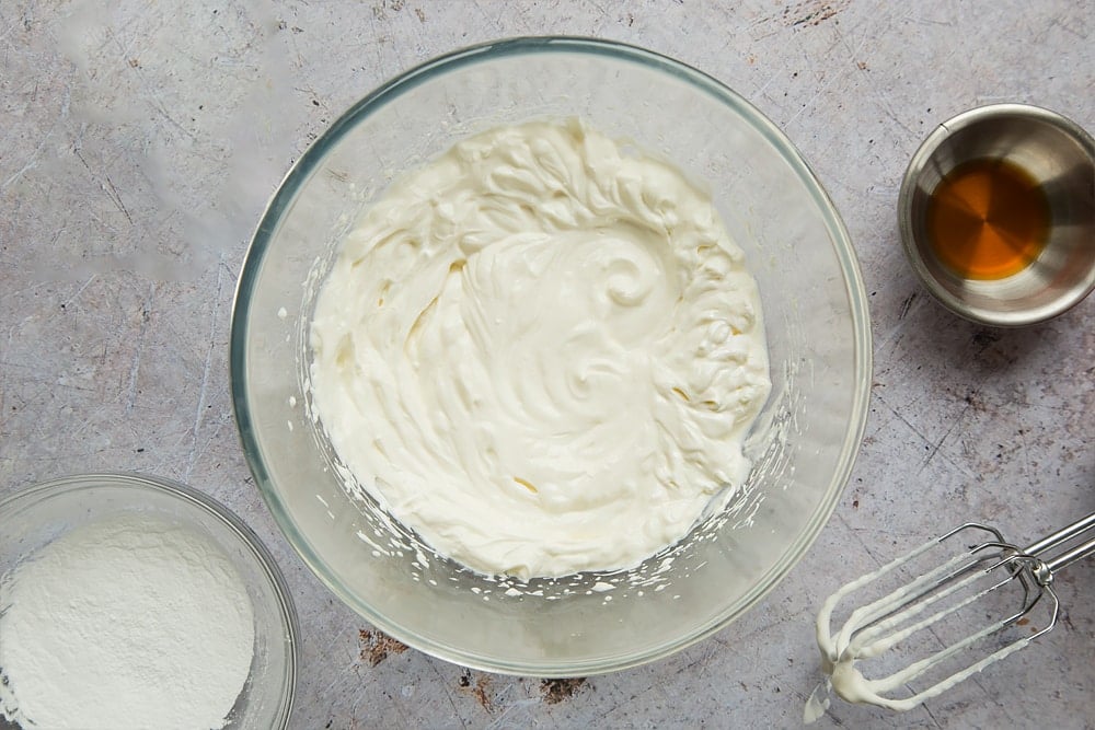 yogurt, sugar and vanilla essence in a large clear bowl whisked together with a whisk on the side.