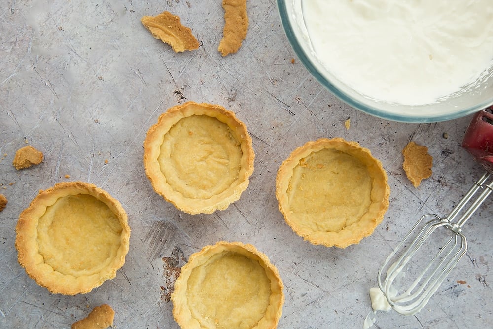 4 cooked pastry cases in a metal pastry tray and a whisk at the side.