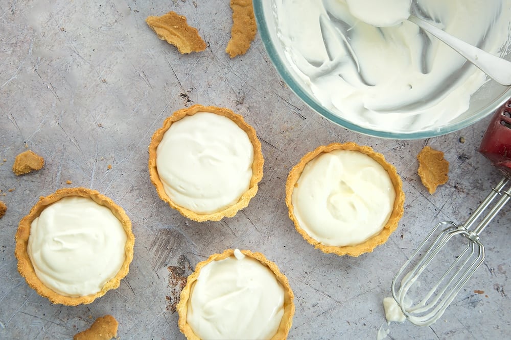 4 small pastry cases filled with whipped yogurt mixture next to a large bowl of yogurt mixture.