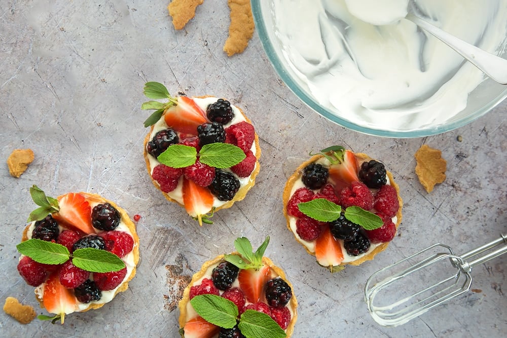 4 small pastry cases filled with whipped yogurt mixture  topped with fresh fruit next to a large bowl of yogurt mixture.