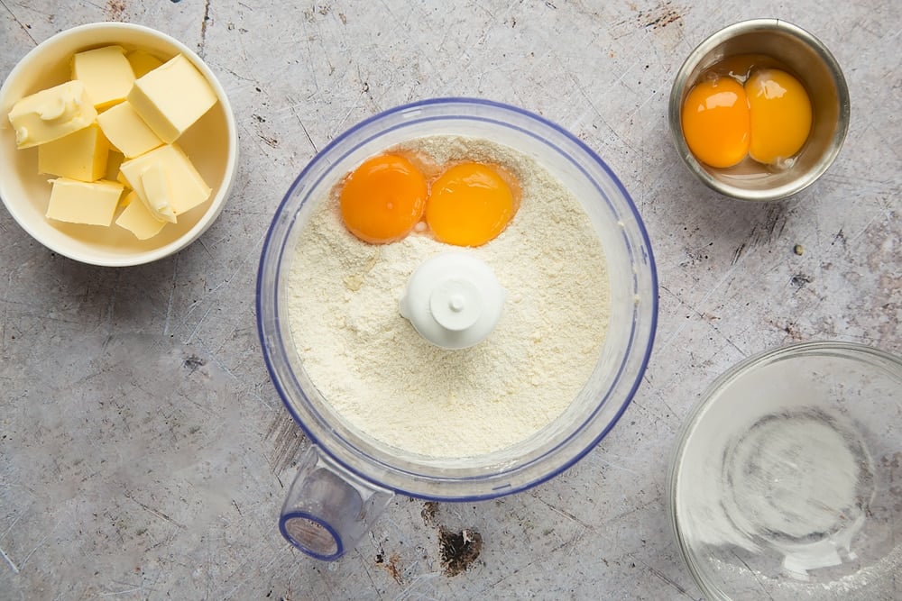 3 egg yolks on a bed of flour in a blender bowl with butter and eggs at either side.