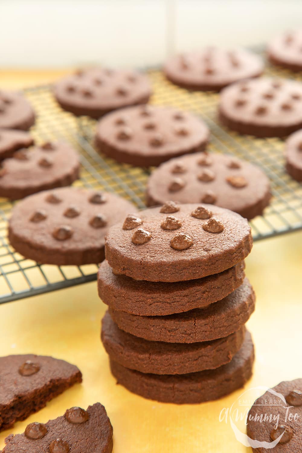 A stack of chocolate shortbread cookies. More cookies cooling on a rack in the background.