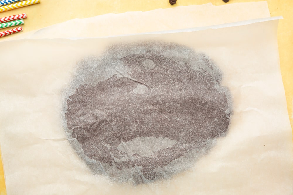 A ball of chocolate shortbread dough pressed between sheets of baking paper. 