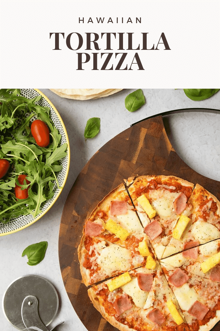 Overhead shot of an hawaiian tortilla pizza on a wooden board with a salad on the side. At the top of the image there's some text describing the image for Pinterest.