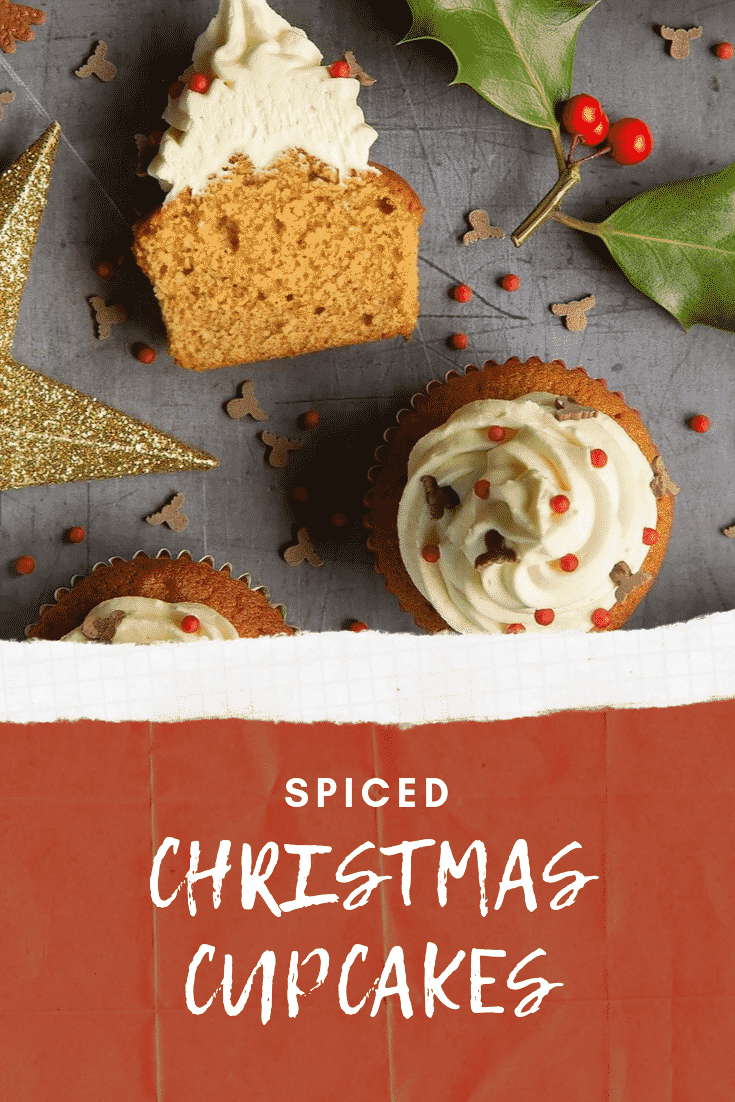 Overhead shot of the finished spiced Christmas cupcakes on a grey table decorated with festive sprinkles. At the bottom of the image there's some white text on a red background describing the image for Pinterest.