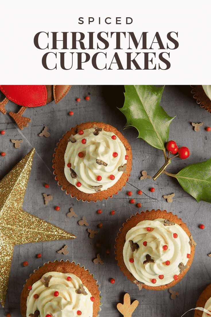 Overhead shot of the finished spiced Christmas cupcakes with marzipan frosting on a grey table. At the top of the image there's some brown text on a white background describing the image for Pinterest.