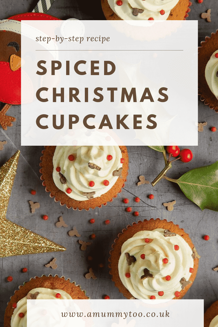 Overhead shot of the finished spiced Christmas cupcakes with marzipan frosting on a grey table decorated with festive ornimants. At the top of the image there's some brown text on a white background describing the image for Pinterest. 