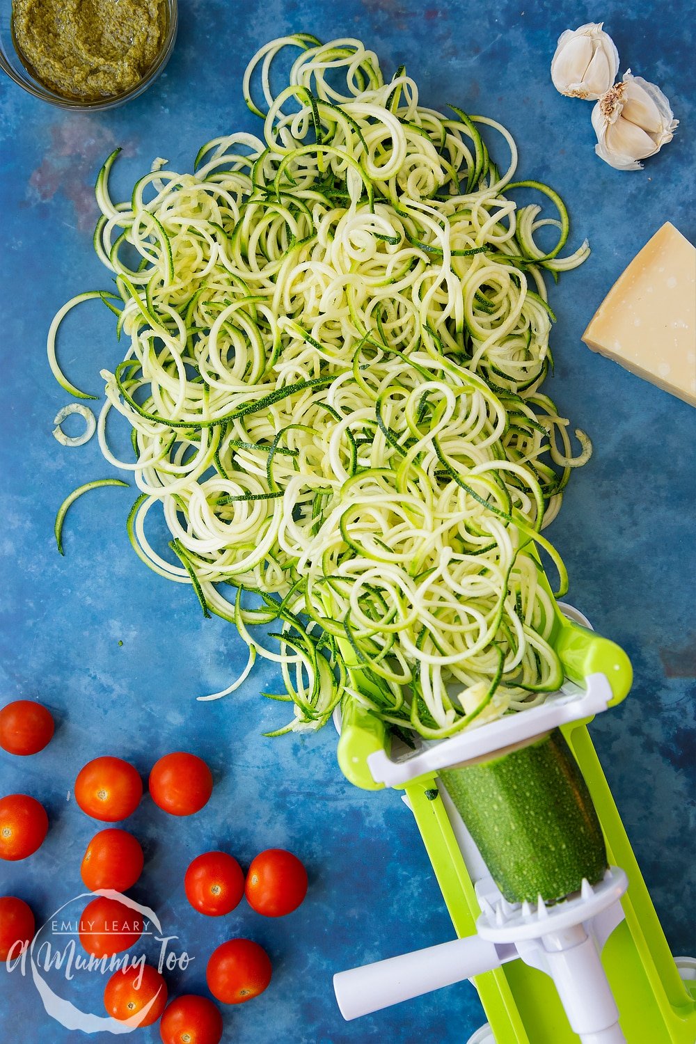 Spiralised courgette coming out of a spiraliser, surrounded by tomatoes, pesto, garlic and Parmesan